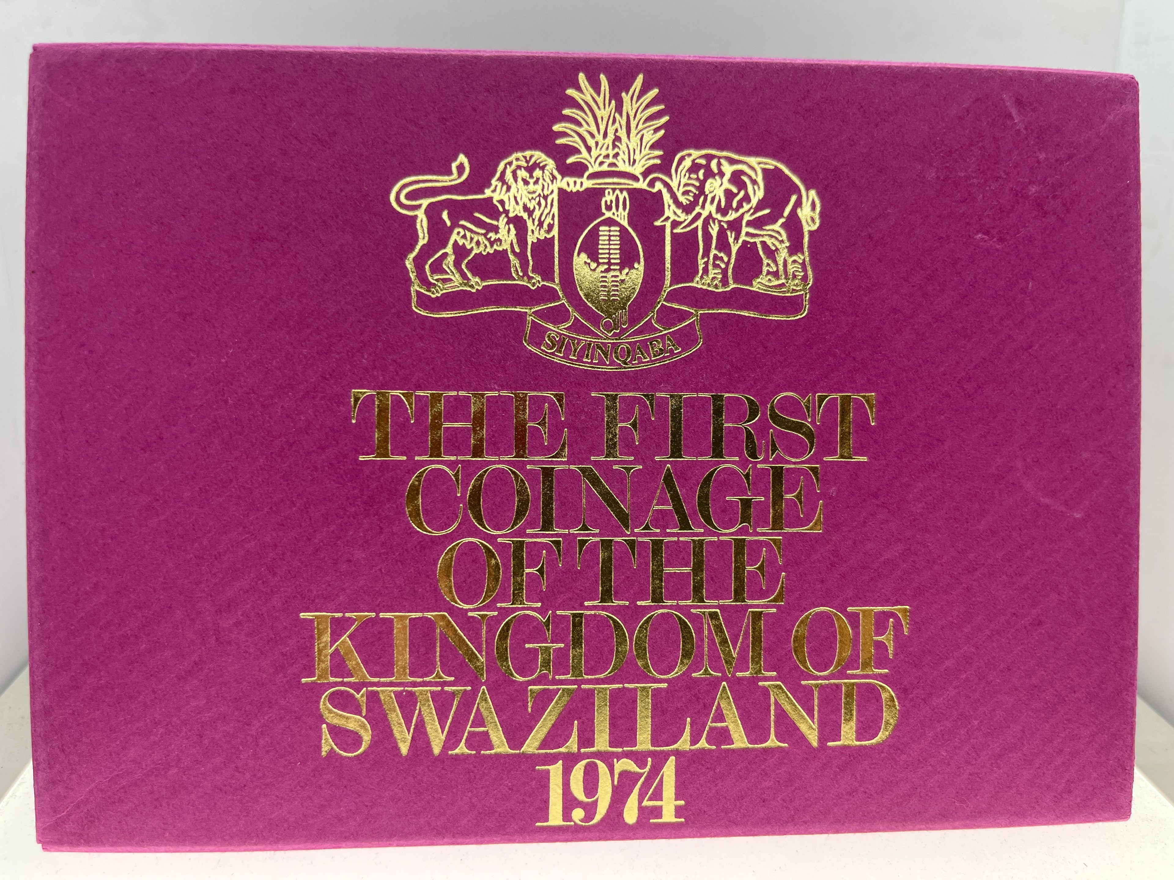 Purple book with gold text and emblem, titled 'The First Coinage of the Kingdom of Swaziland 1974'.